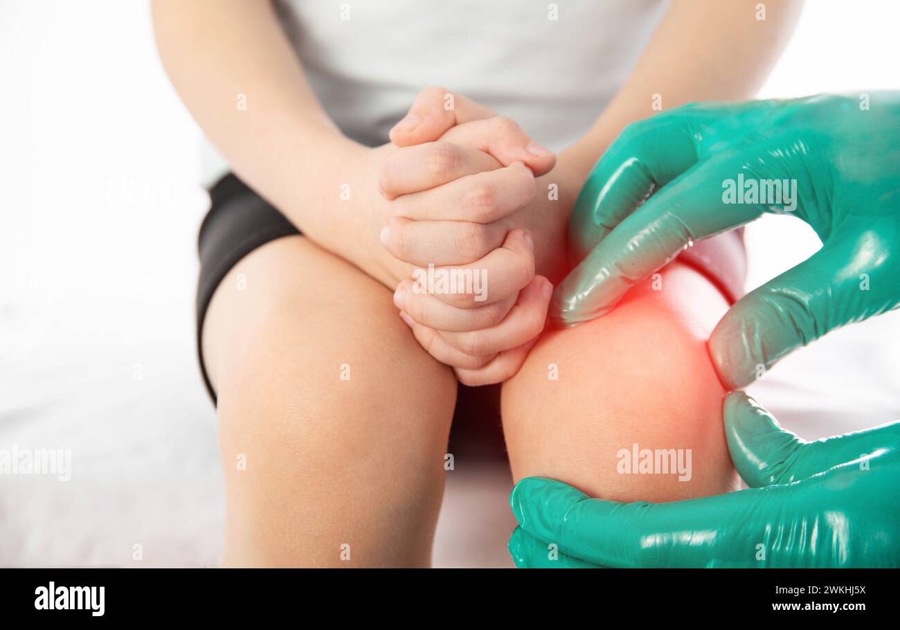 A doctor traumatologist orthopedist examines the knee joint of a child who has knee pain. Concept of growing pains in children. Dislocation and injury Stock Photo