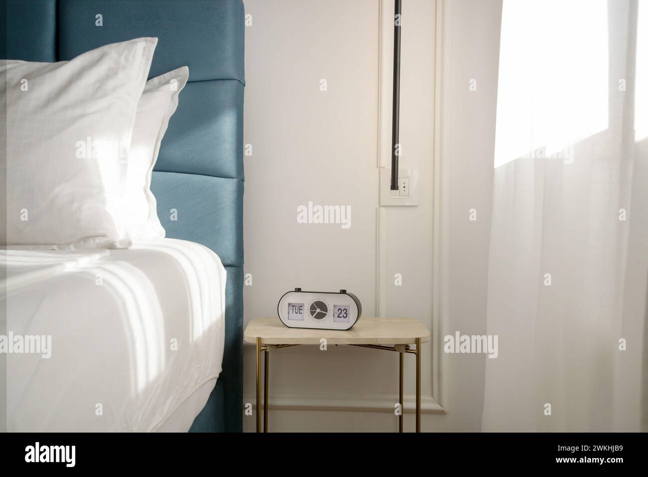 Blue king size bed with crisp white bedding and digital alarm clock on the nightstand under beautiful morning sunlights Stock Photo