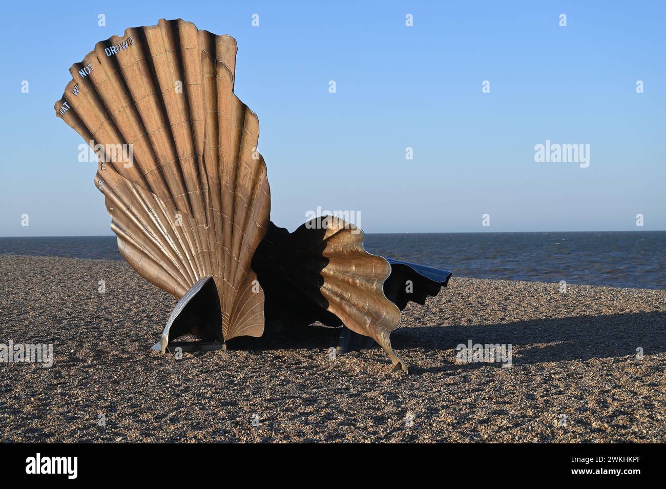 An aged seashell rests gently on the sandy shore, near the tranquil waters Stock Photo