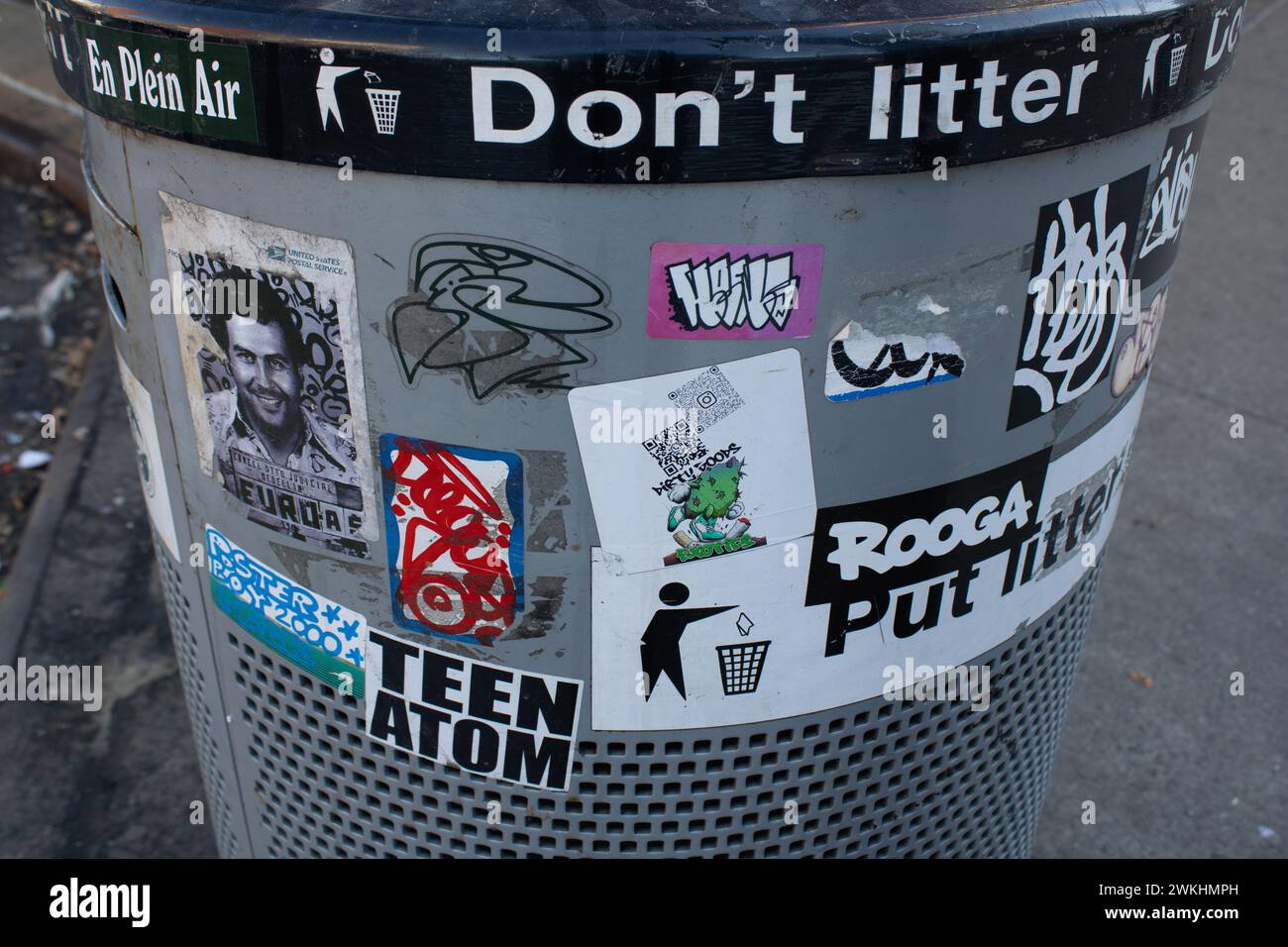 A gray trashcan adorned with colorful stickers and photographs Stock Photo