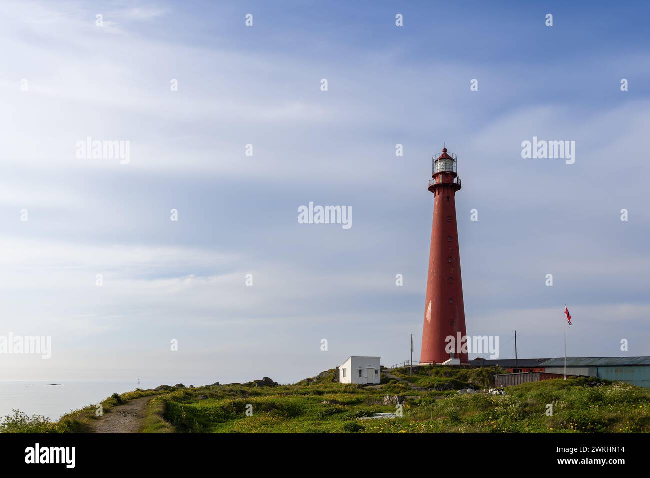 A serene summer day at Andenes Lighthouse in Norway, with the sea in the background and the national flag proudly on display. Stock Photo