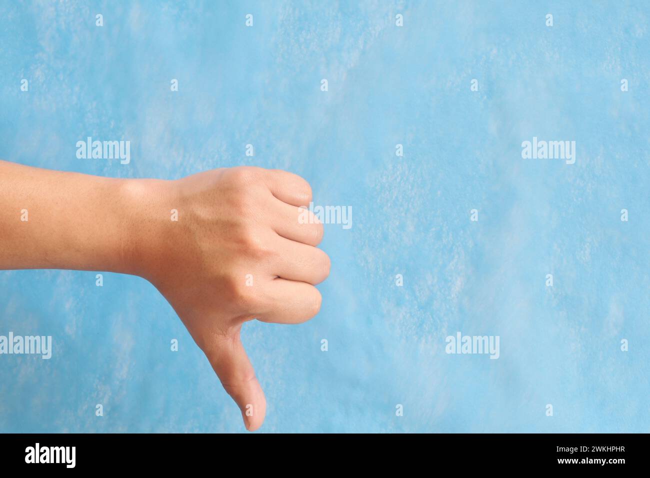 Young male Asian hand making thumbs down sign isolated on blue background. Stock Photo