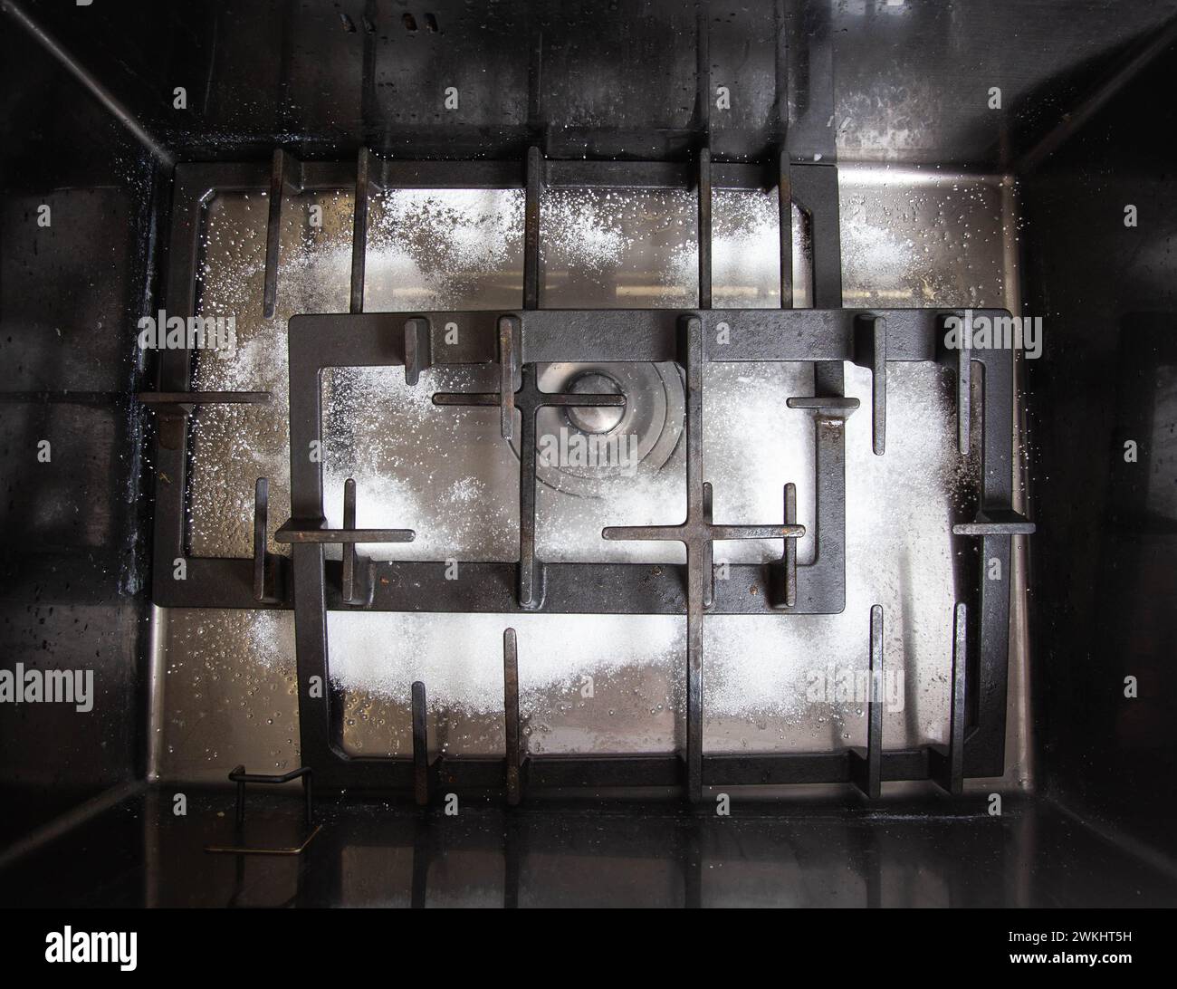 Dirty gas stove grates in the sink with a modern oxygen cleaner for