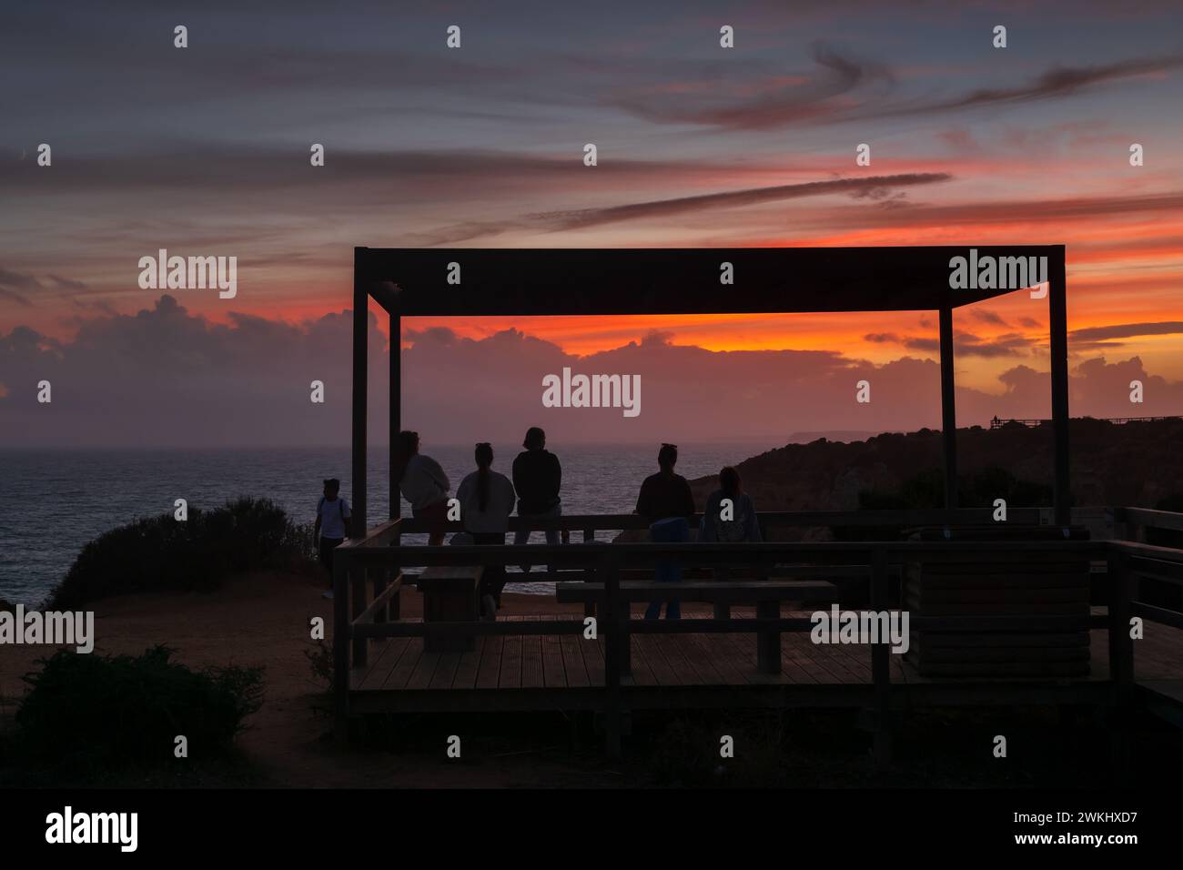 Group of friends enjoy tranquil sunset by the Atlantic Ocean from a viewpoint on the Algarve coast in Lagos, Portugal. Stock Photo
