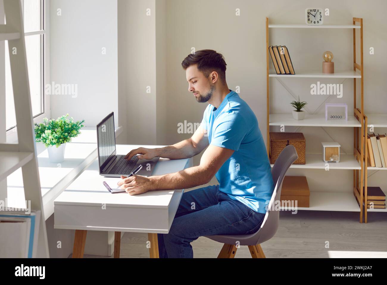 Young man writing notes while using laptop at home Stock Photo