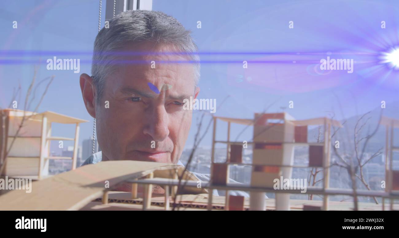 Image of blue light beams and lens flare over male architect looking at architectural model Stock Photo