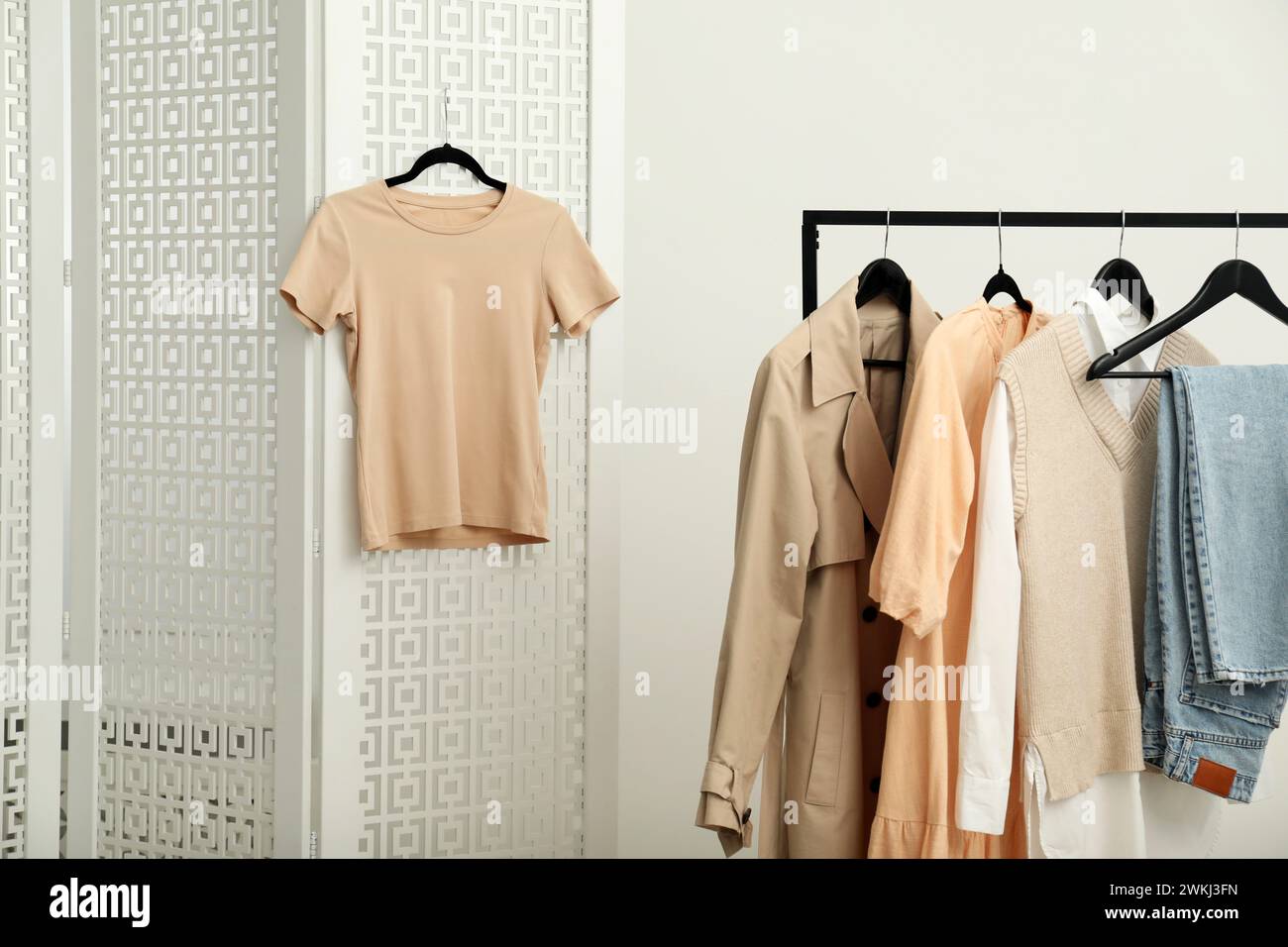 Beige t-shirt hanging on folding screen near rack with stylish women's clothes indoors Stock Photo