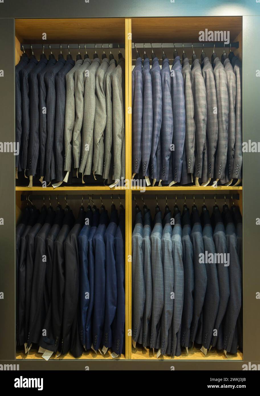 A row of men's suits, jackets hanging on a rack for display. Elegant man suit jackets hanging in a row on hangers. Stock Photo