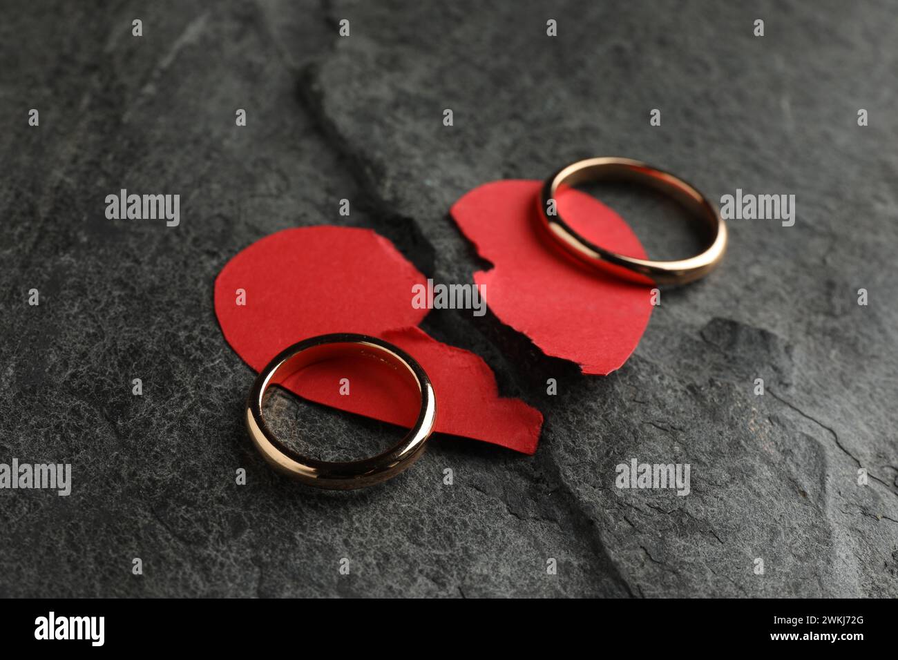 Halves of torn red paper heart and wedding rings on dark grey table ...