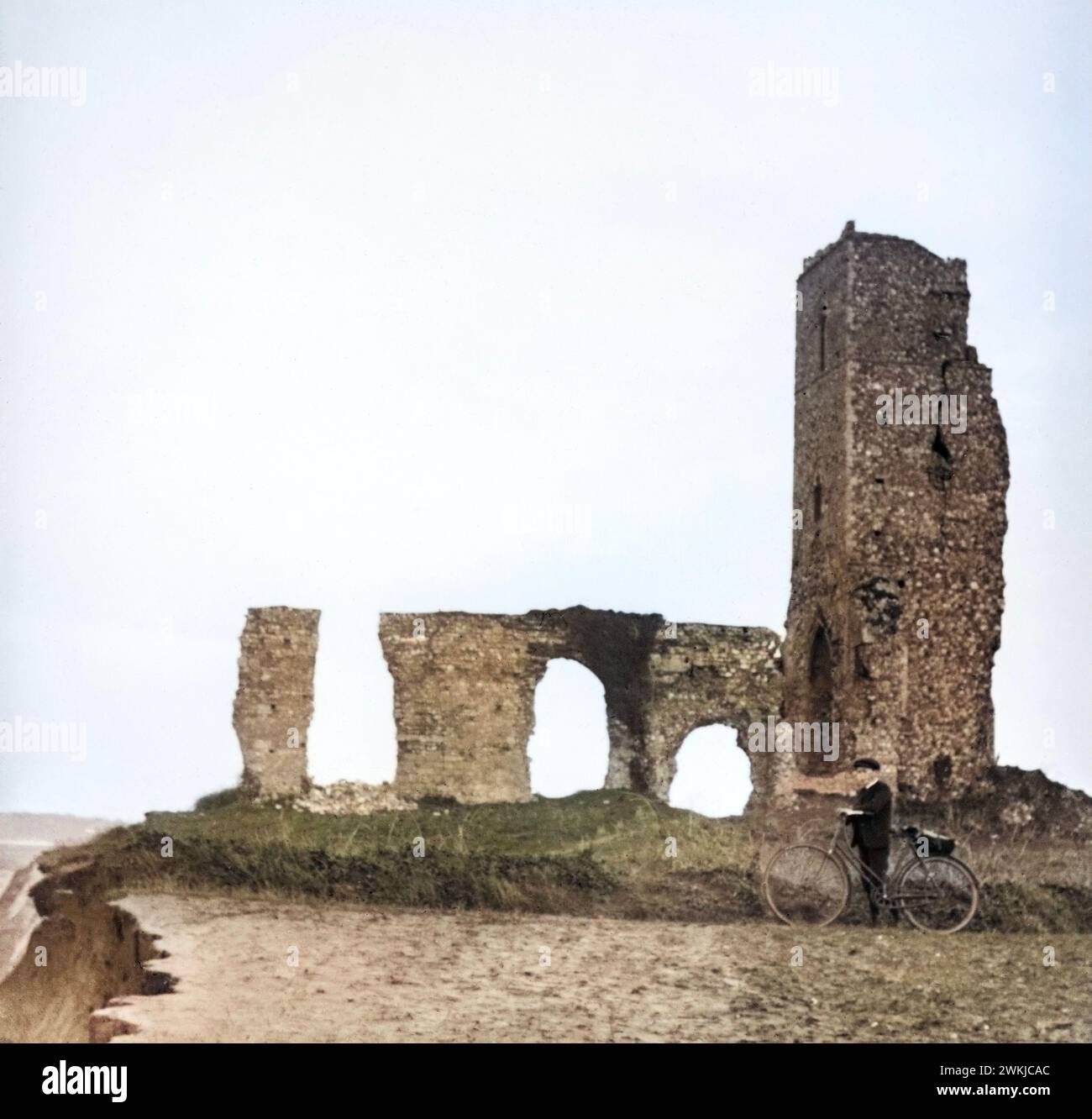 Colourised magic lantern slide of boy with bicycle standing by ruins of All Saints church, Dunwich, Suffolk, England, UK c 1900 Stock Photo