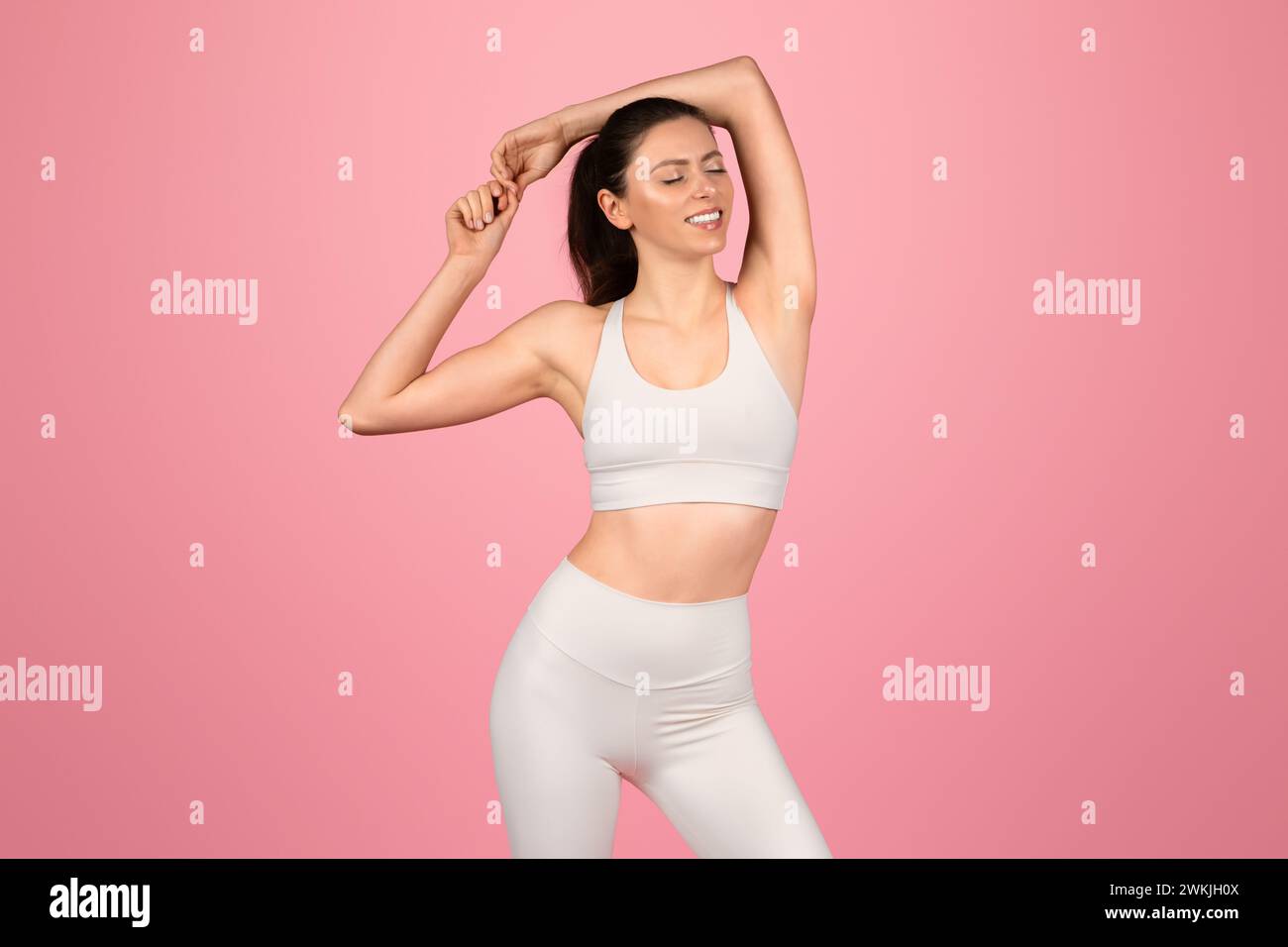 Graceful woman in white athletic apparel enjoying a stretch, eyes closed with a contented smile Stock Photo