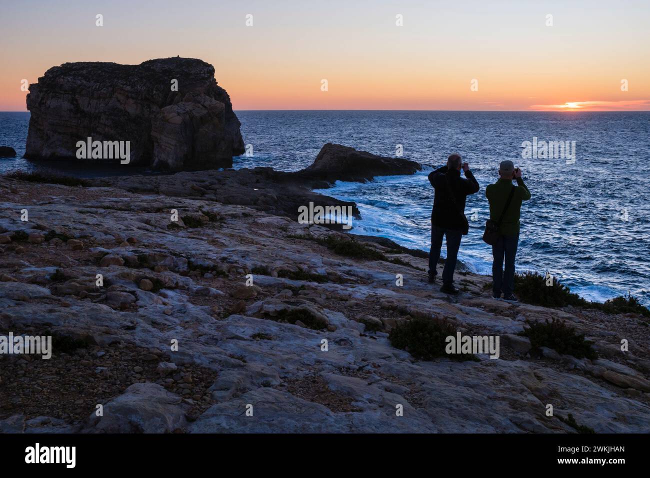 Tourists photographing the sunset at Fungus Rock, Dwejra Bay, Gozo, Malta Stock Photo