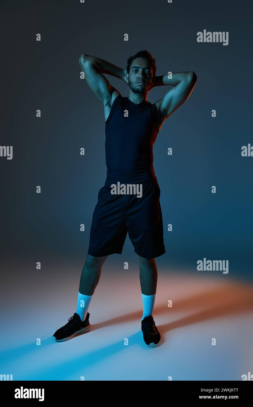 good looking african american man in sportwear posing with arms above head on dark background Stock Photo