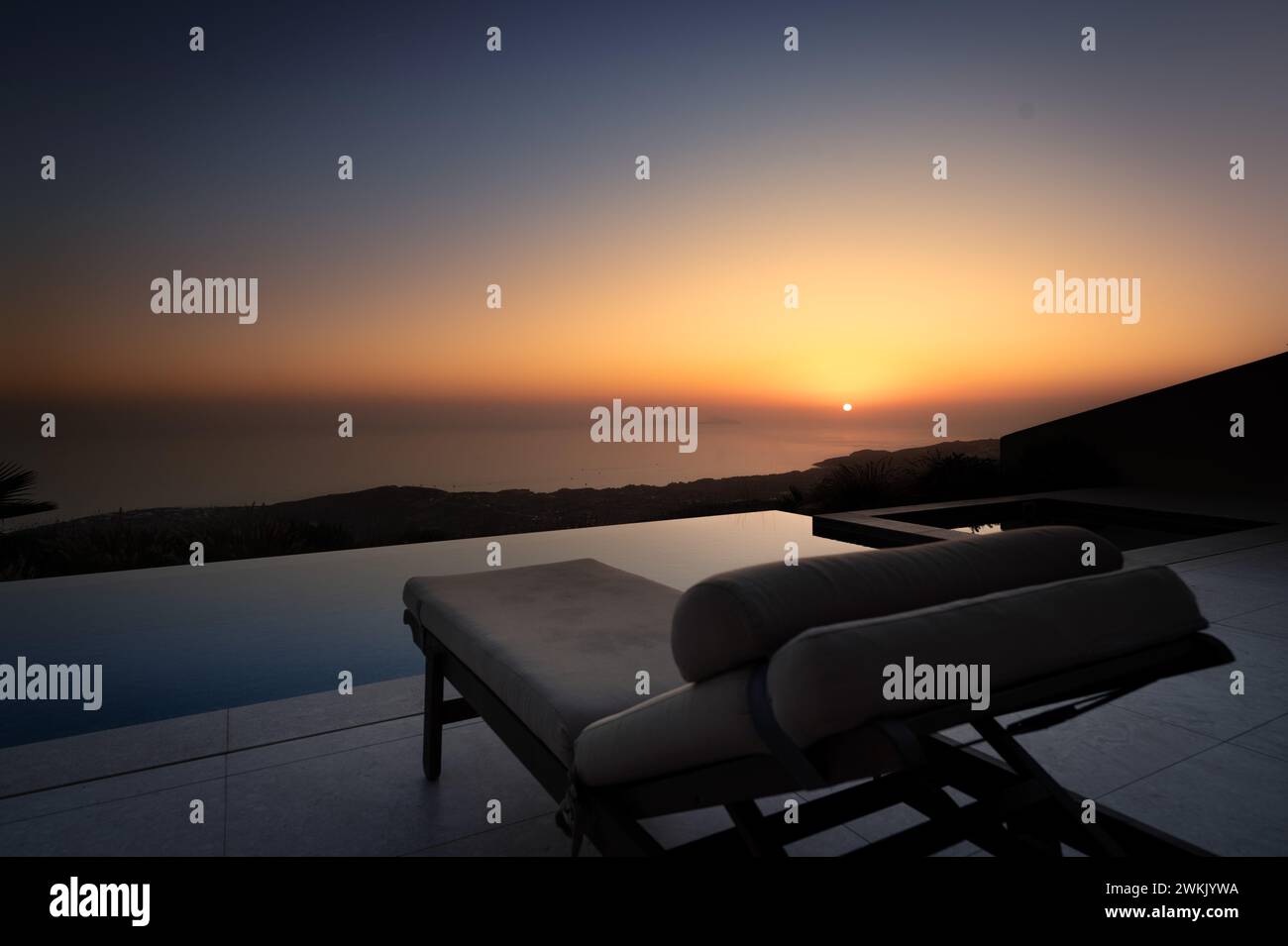 Twilight Serenity: Sun Setting Over Ocean View Pool Stock Photo