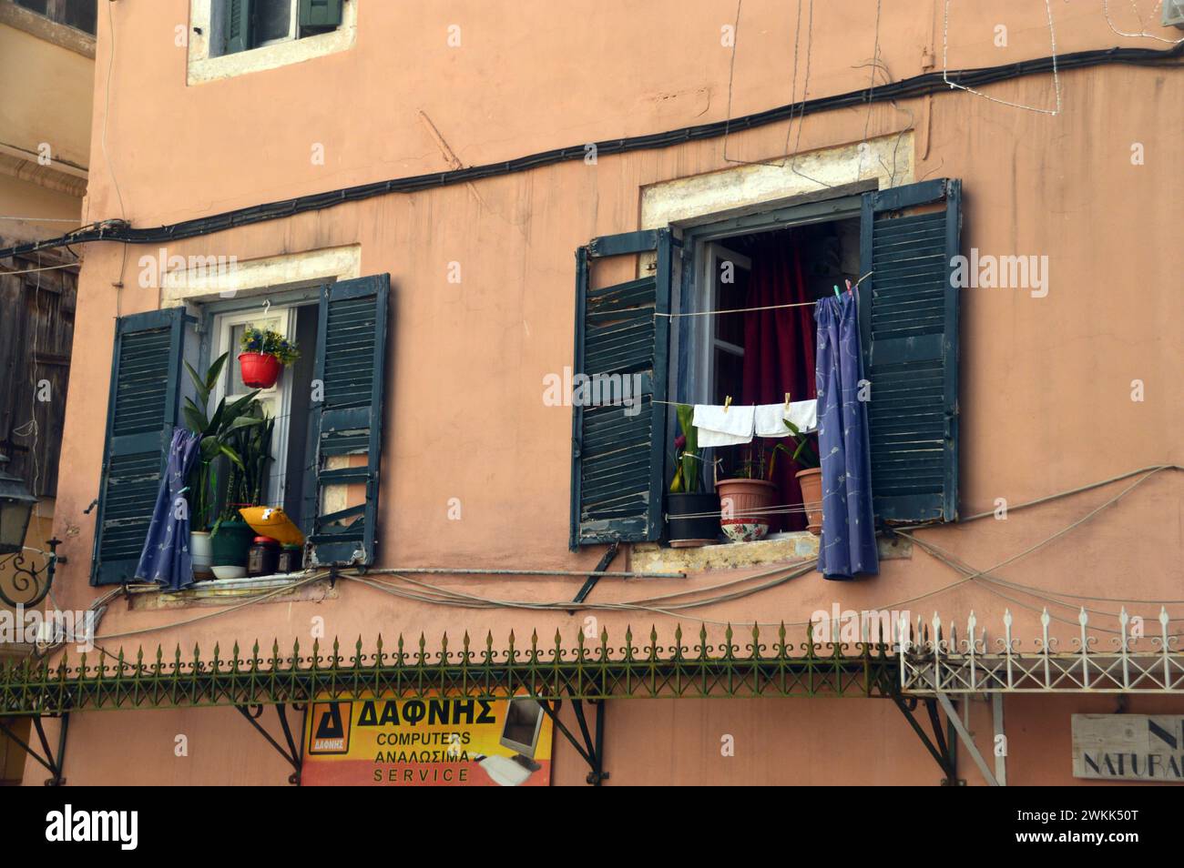 Washing Hanging on Clothes Line Outside Green Shuttered Windows Above Shops in the Old Town of Corfu, Greece, EU. Stock Photo