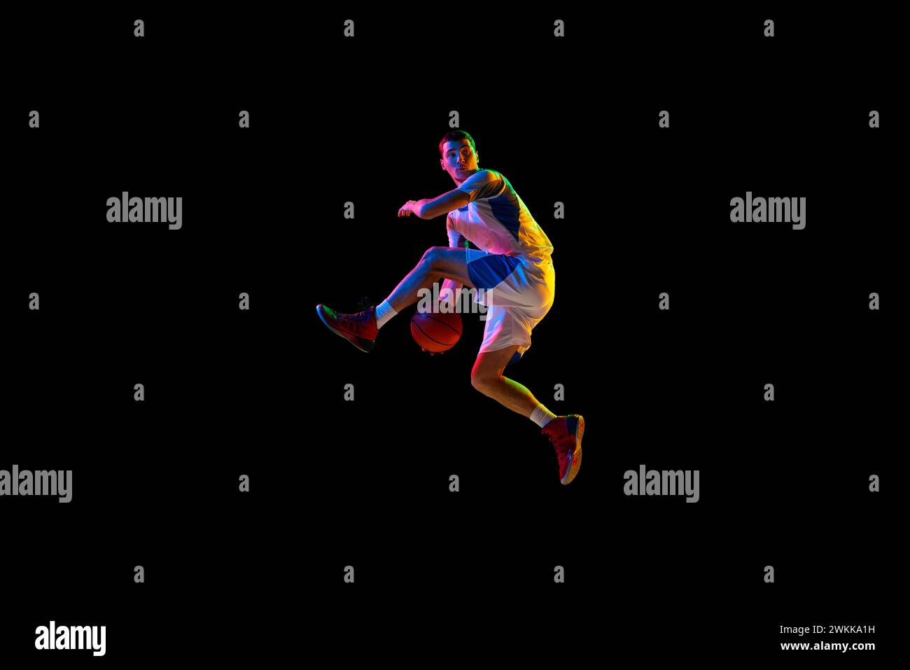 Action shot of basketball player's crossover dribble against black studio background in mixed neon light. Stock Photo