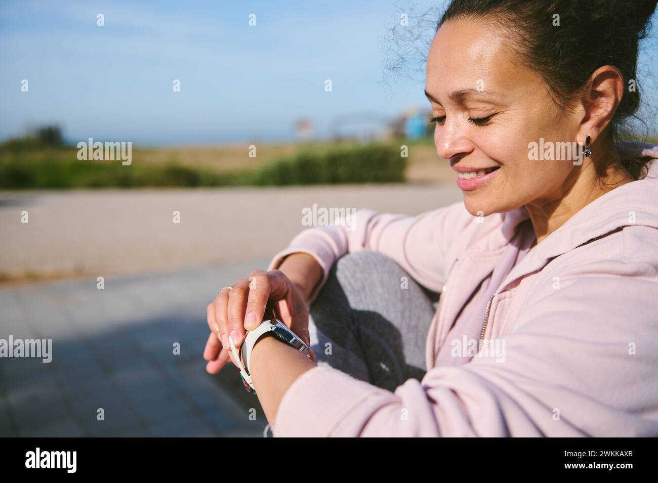Close-up portrait of a happy smiling young Latin American woman setting up her smartwatch while working out outdoor. Caucasian woman checking her work Stock Photo