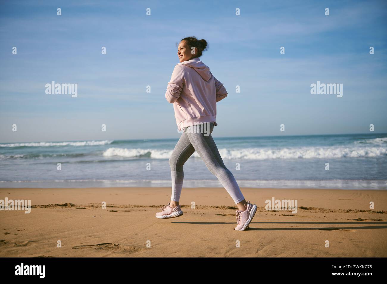 Portrait of middle aged multi ethnic happy active sportswoman running along the Atlantic beach. Healthy fitness woman jogging outdoors. Sports and hea Stock Photo