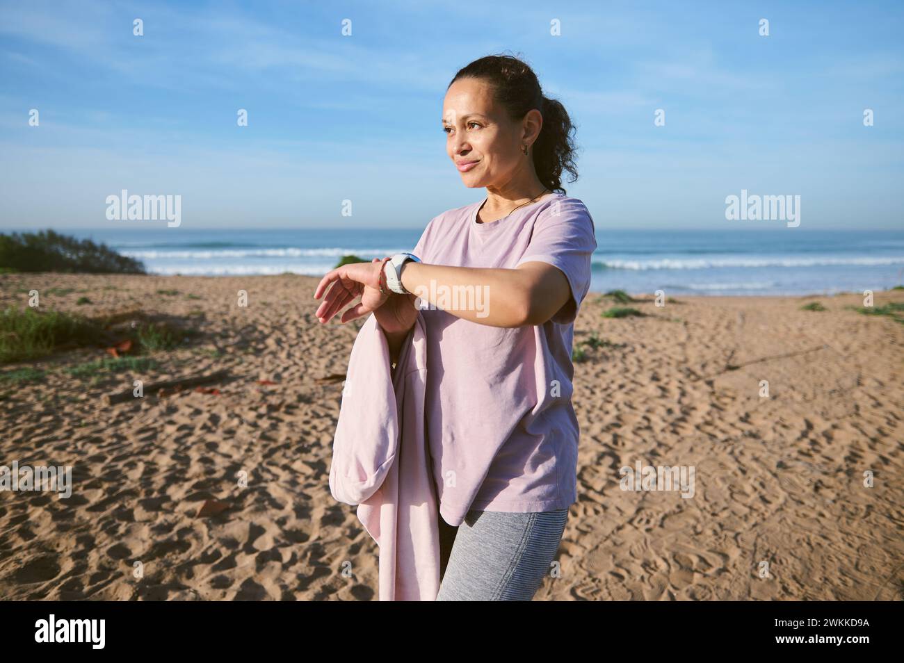 Happy female athlete wearing activewear and checking her pulse rate with smartwatch while outdoors exercising. Happy female athlete wearing sports wea Stock Photo