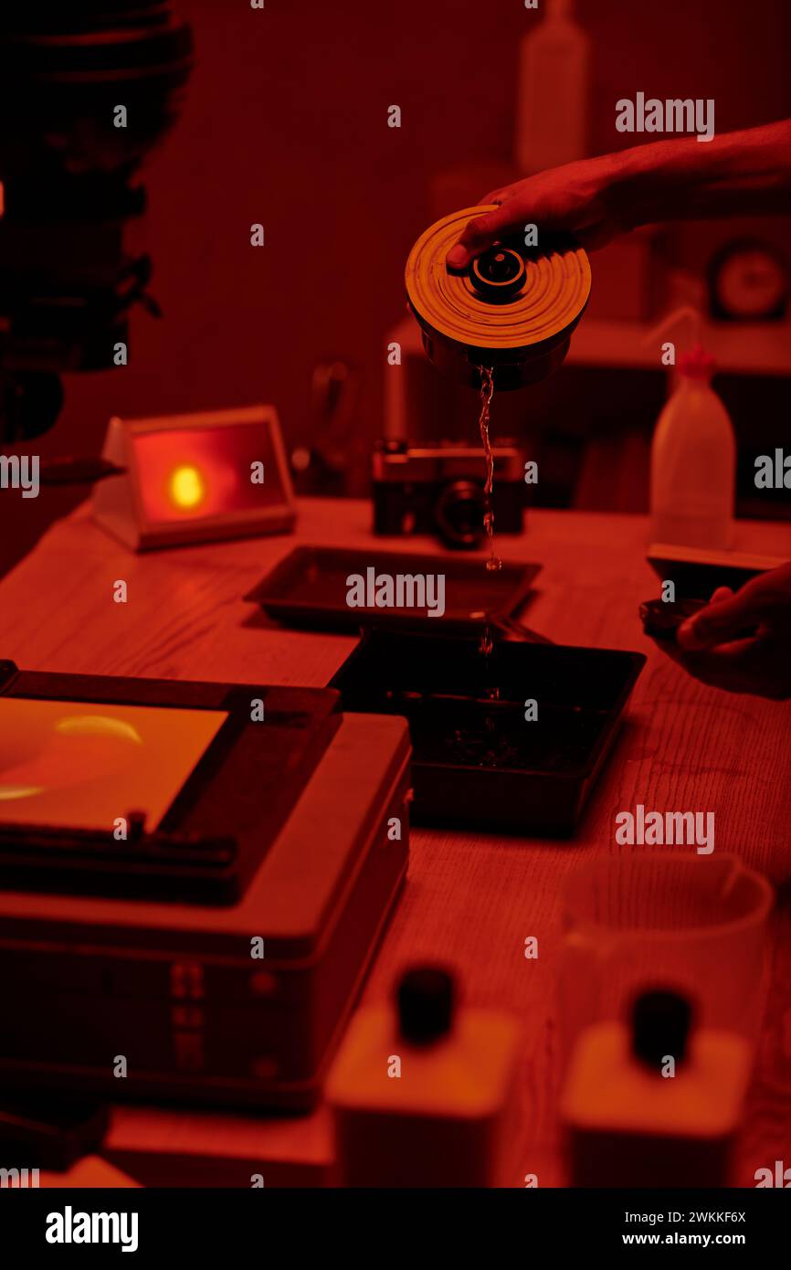 cropped view of photographer pours developer liquid for film processing, red darkroom Stock Photo