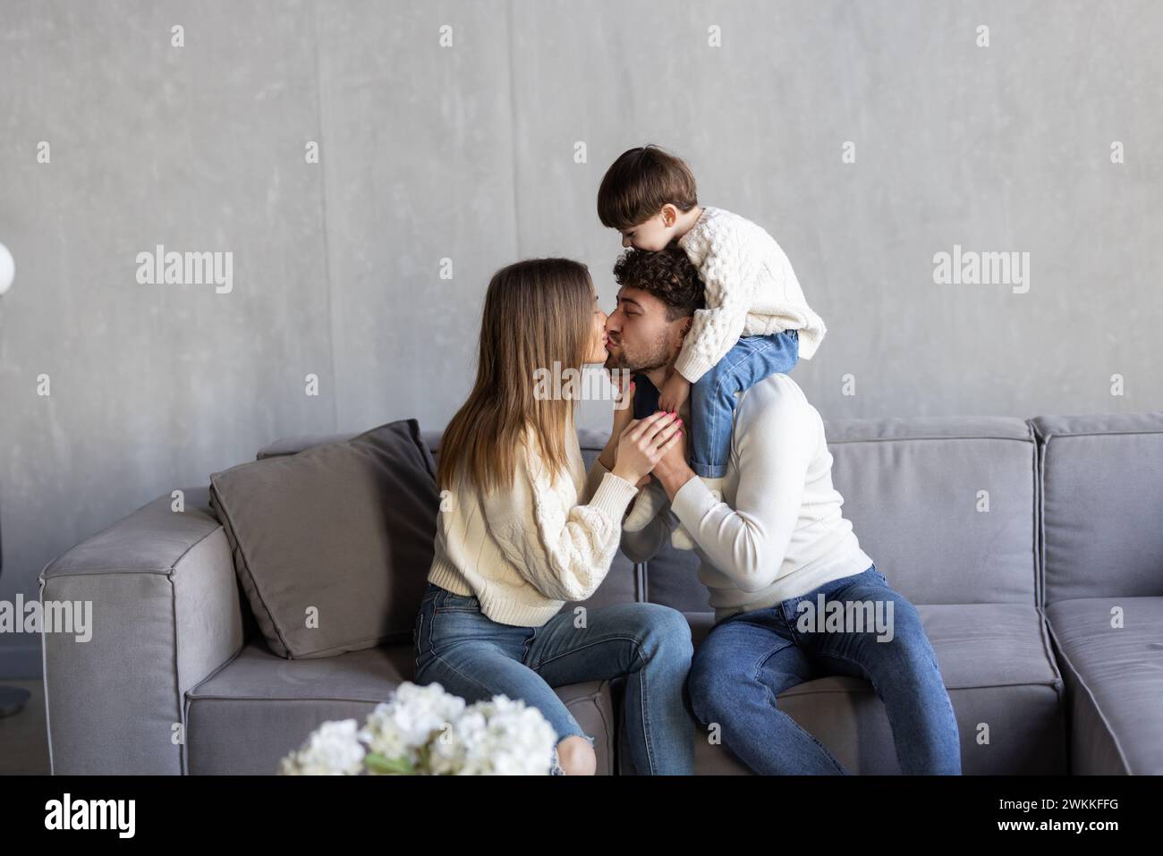 Happy young Caucasian family with small 7s son relax on sofa in living room use modern smartphone together. Smiling parents with little boy child talk Stock Photo