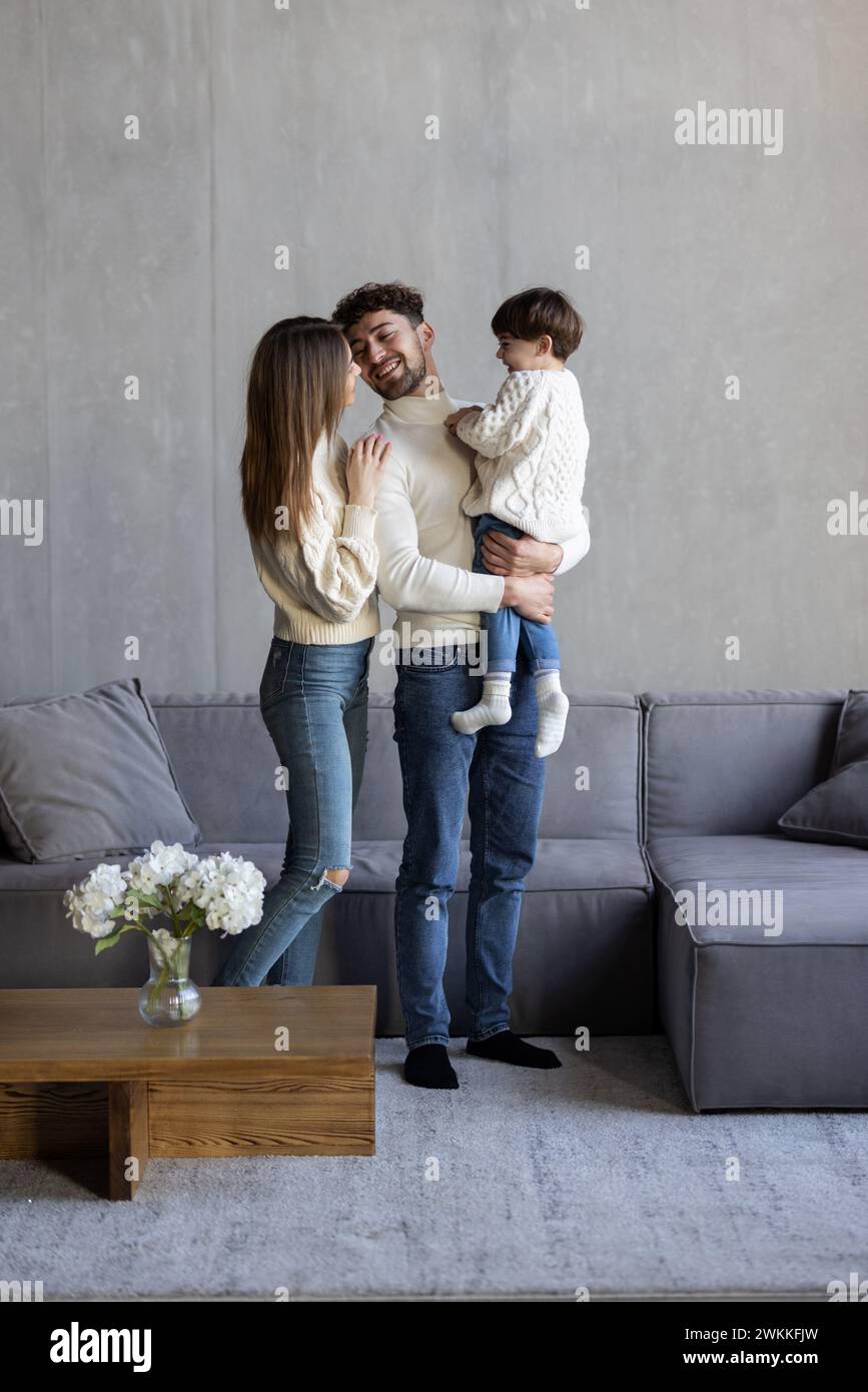 Happy young bearded man cuddling sitting on cozy couch beautiful wife with son. Stock Photo
