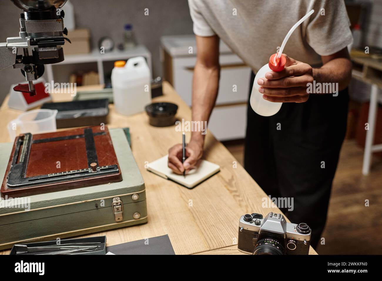 cropped dark skinned photographer prepares chemicals for film development and taking notes Stock Photo