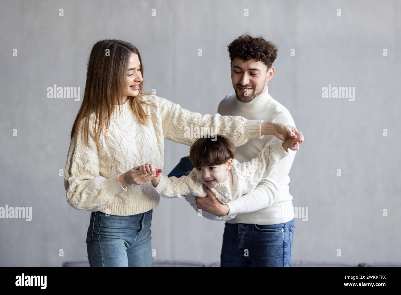 Full body father and mother smiling and lifting mixed race son near couch Stock Photo