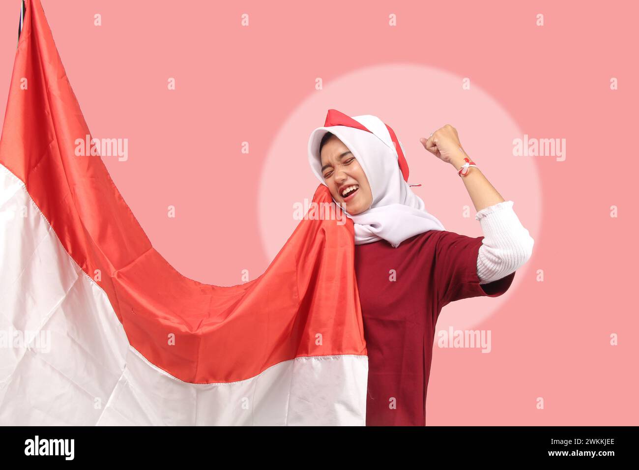 young asian woman celebrating happy independence of republic of indonesia in red and white satin with smiling expression on pink background, clipping Stock Photo