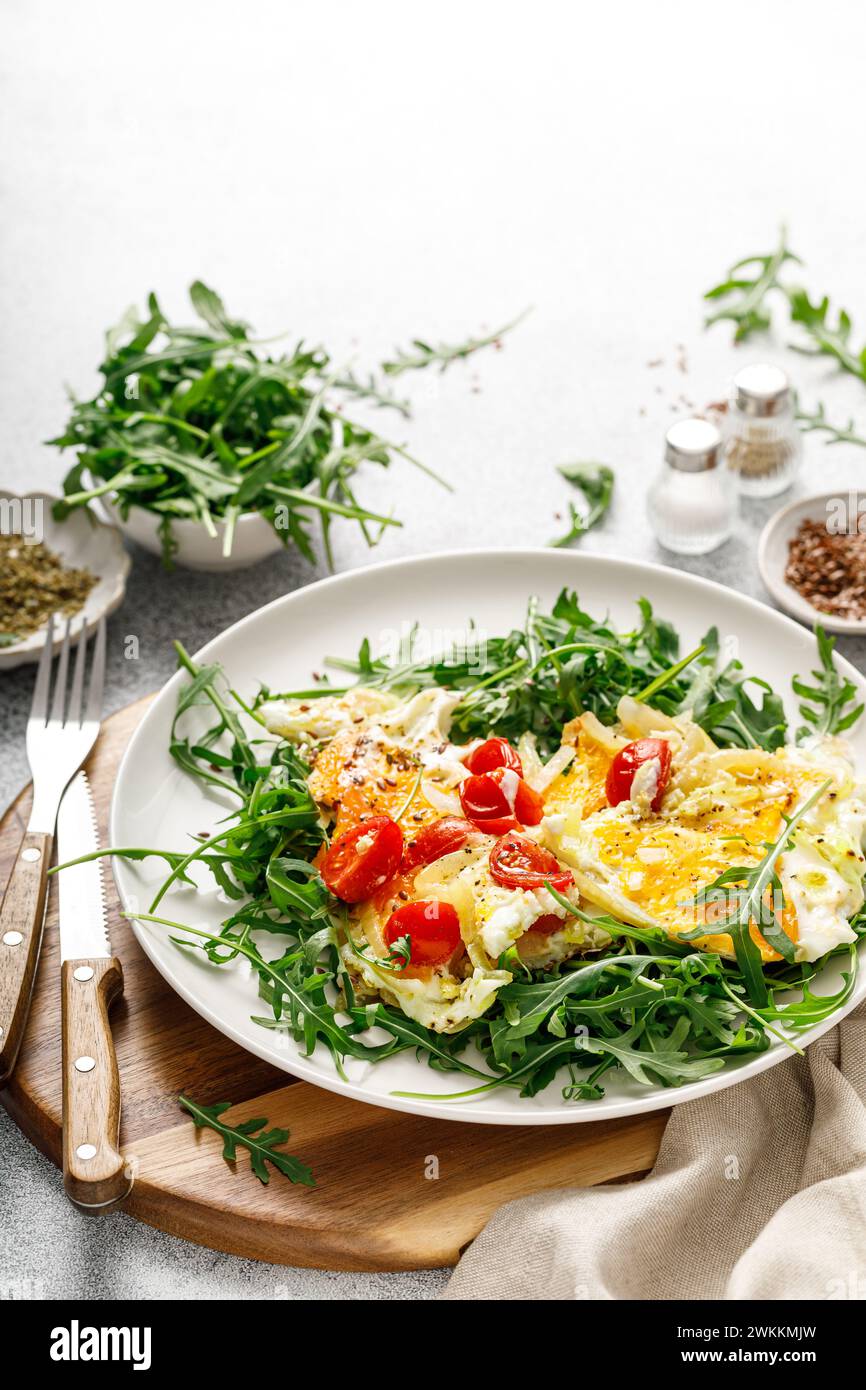 Fried eggs, omelette with onions, tomatoes and fresh arugula salad Stock Photo