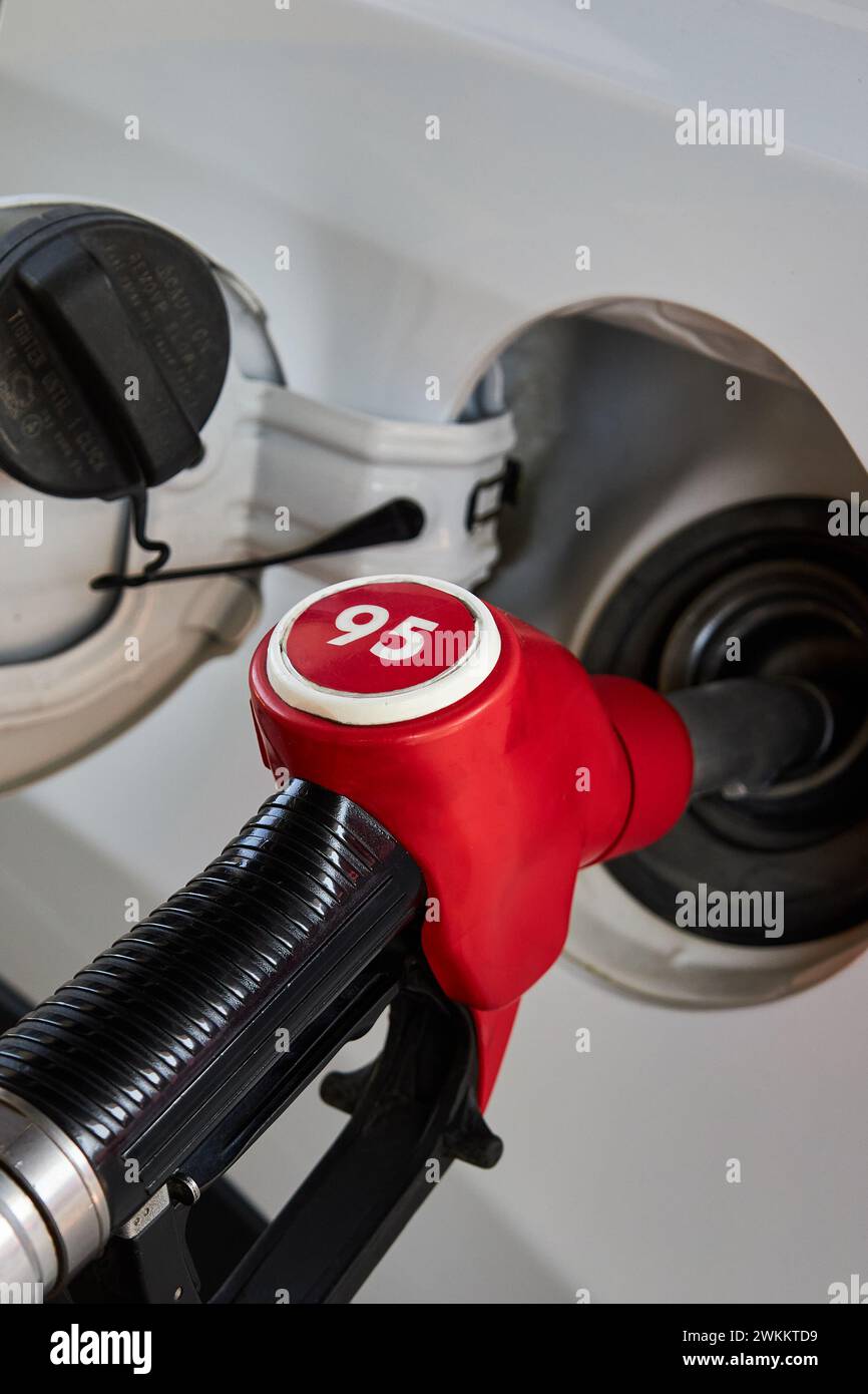 Car refueling process. Gasoline dispenser, Red fuel pump nozzle unit inserted into the gas tank of a white automobile. Refueling gun, 95 petrol benzin Stock Photo