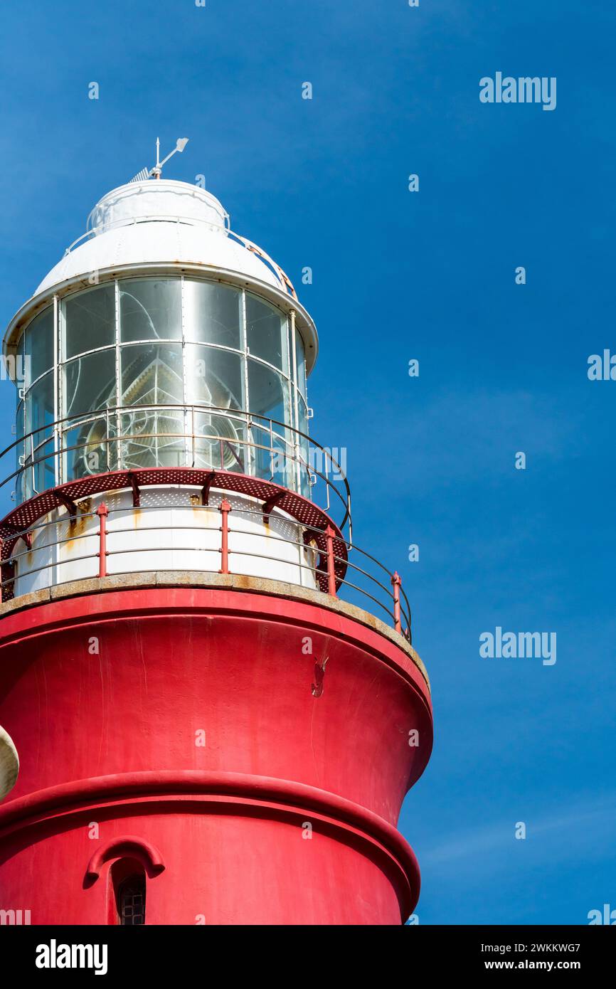 close up view of the top of a lighthouse showing the lantern and glass dome against a blue sky concept technology and coastal safety Stock Photo