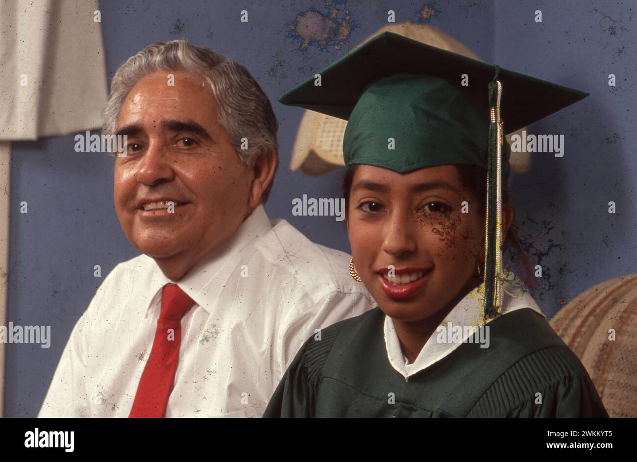 San Antonio Texas USA, 1990: Female high school senior wearing cap and gown sits with her father at home before her commencement ceremony from Edgewood High School. Her father, Demetrio Rodriguez, is the named plaintiff in Rodriguez v. San Antonio Independent School District, which led to the landmark Edgewood v. Kirby lawsuit that forced the state of Texas to make its funding of public schools more equitable between districts serving rich and white students and those serving poor and minority students.  MR ES-0122 Model Released  ©Bob Daemmrich Stock Photo