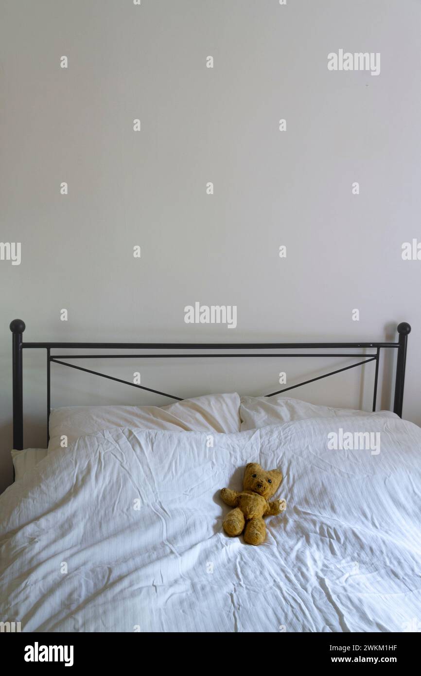 A portrait orientated image of an old teddy bear lying on a bed with an