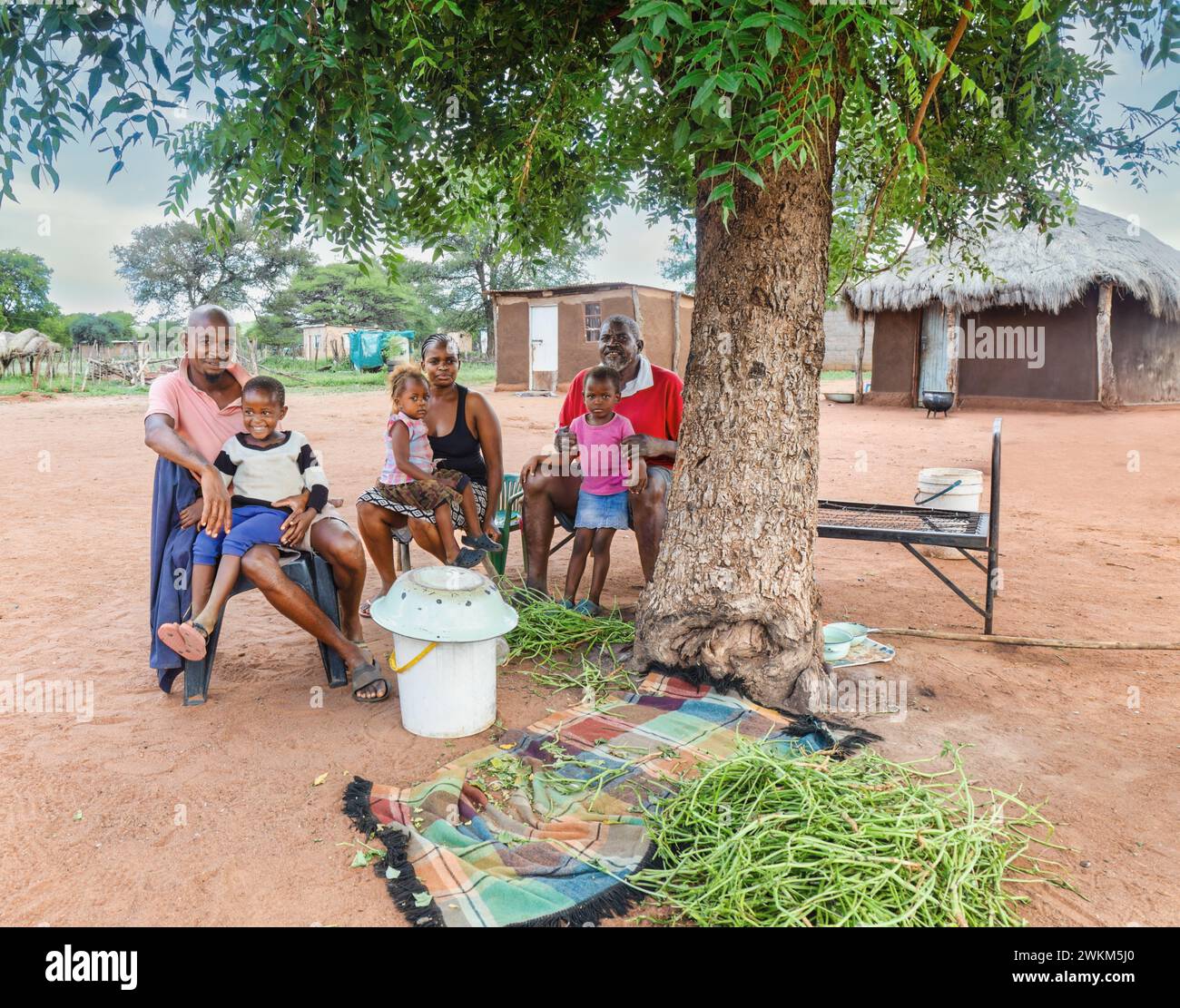 village happy extended multi generation african family , sited on chairs in the outdoors kitchen, in front of the mud hut with thatched roof Stock Photo