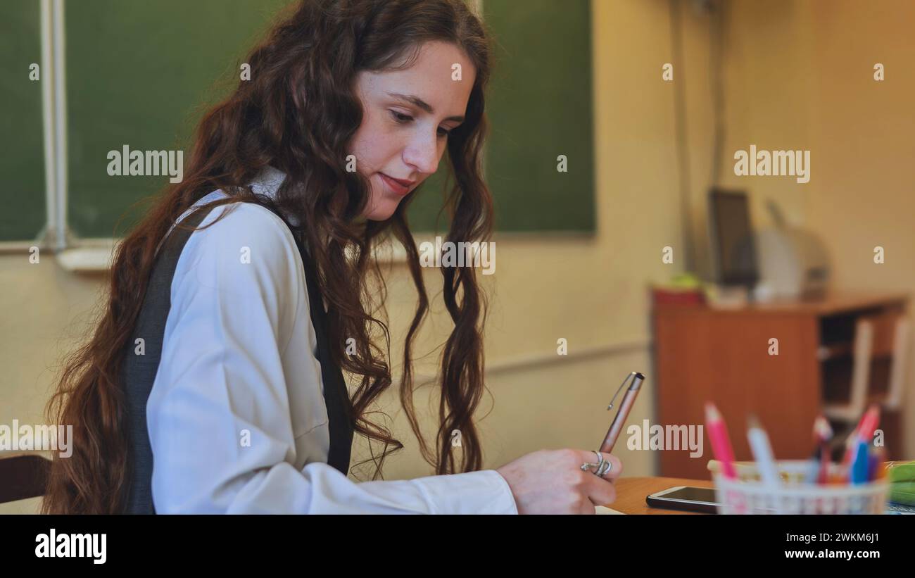 Schoolgirl as a teacher sits at a desk and writes something Stock Photo ...