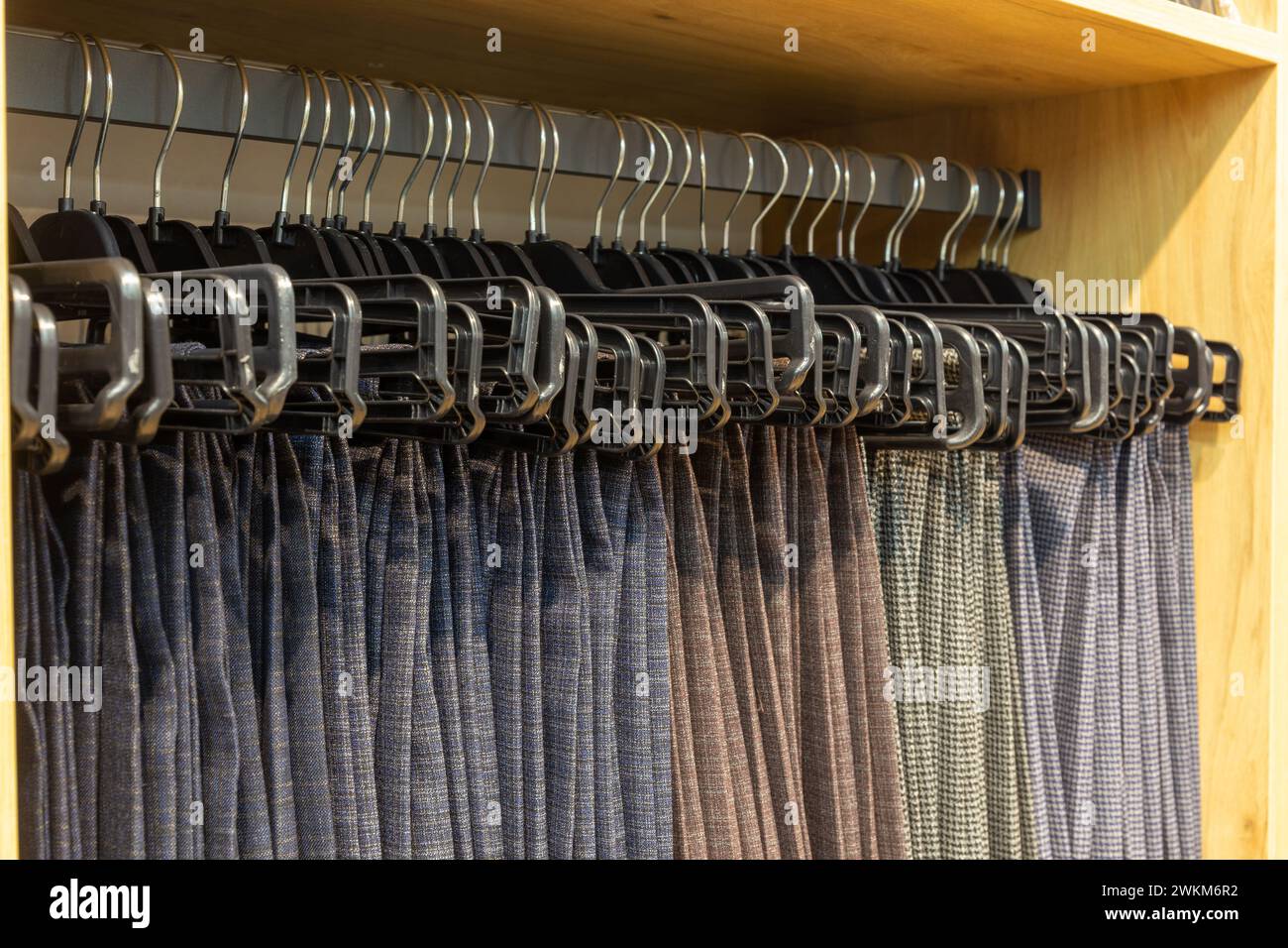 Men's classic trousers on hangers in a boutique. Showcase with many men's trousers hanging on hangers in stock on hangers in a men's clothing store. Stock Photo