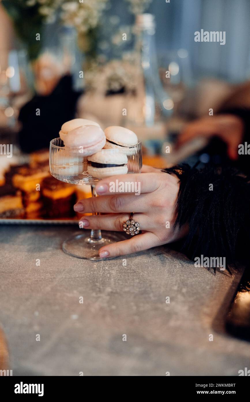 A person presenting a glass filled with vanilla flavoured macarons on a table Stock Photo