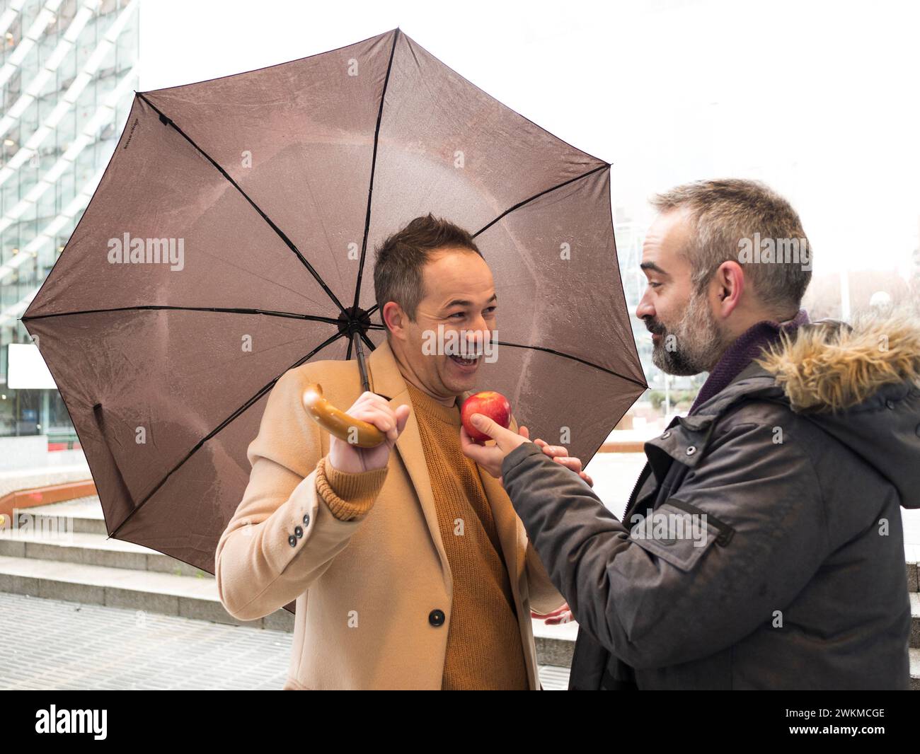 couple of executives offer each other apple on the street in the rain in winter Stock Photo
