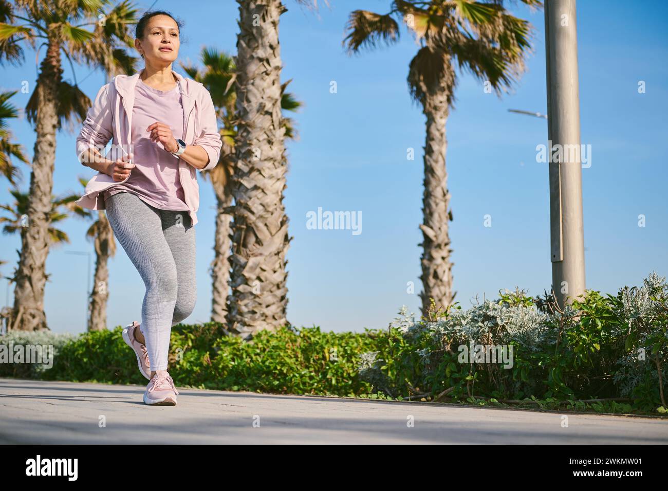 Full length portrait of young woman runner jogging on the treadmill, enjoying a marathon of Breast Cancer Awareness campaign. Pink October. Sport, emp Stock Photo
