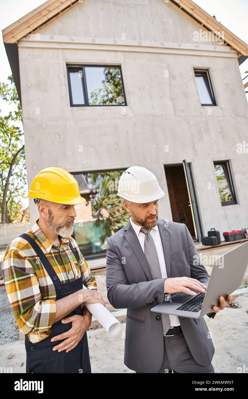 handsome architect and builder in overalls and suit working with laptop ...