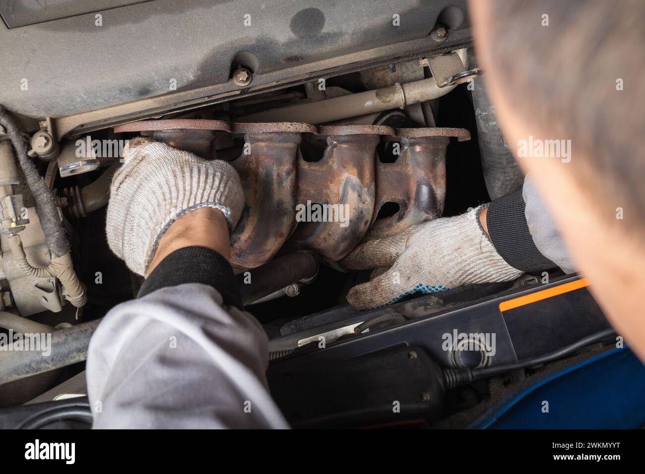An auto mechanic installs an exhaust manifold to collect and remove