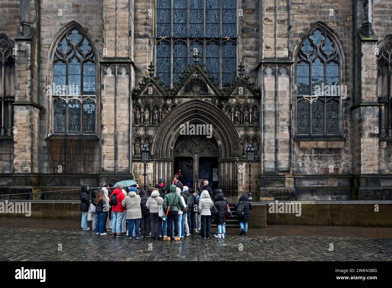 Tourists on a walking tour of Edinburgh's Old Town standing outside St Giles Cathedral on a wet spring morning. Stock Photo