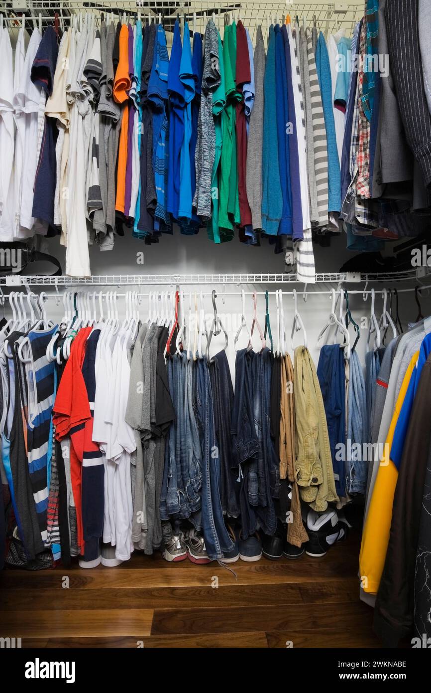 T-shirts, sweaters, blue jeans on hangers and shoes inside teenager's walk-in closet inside luxurious home. Stock Photo