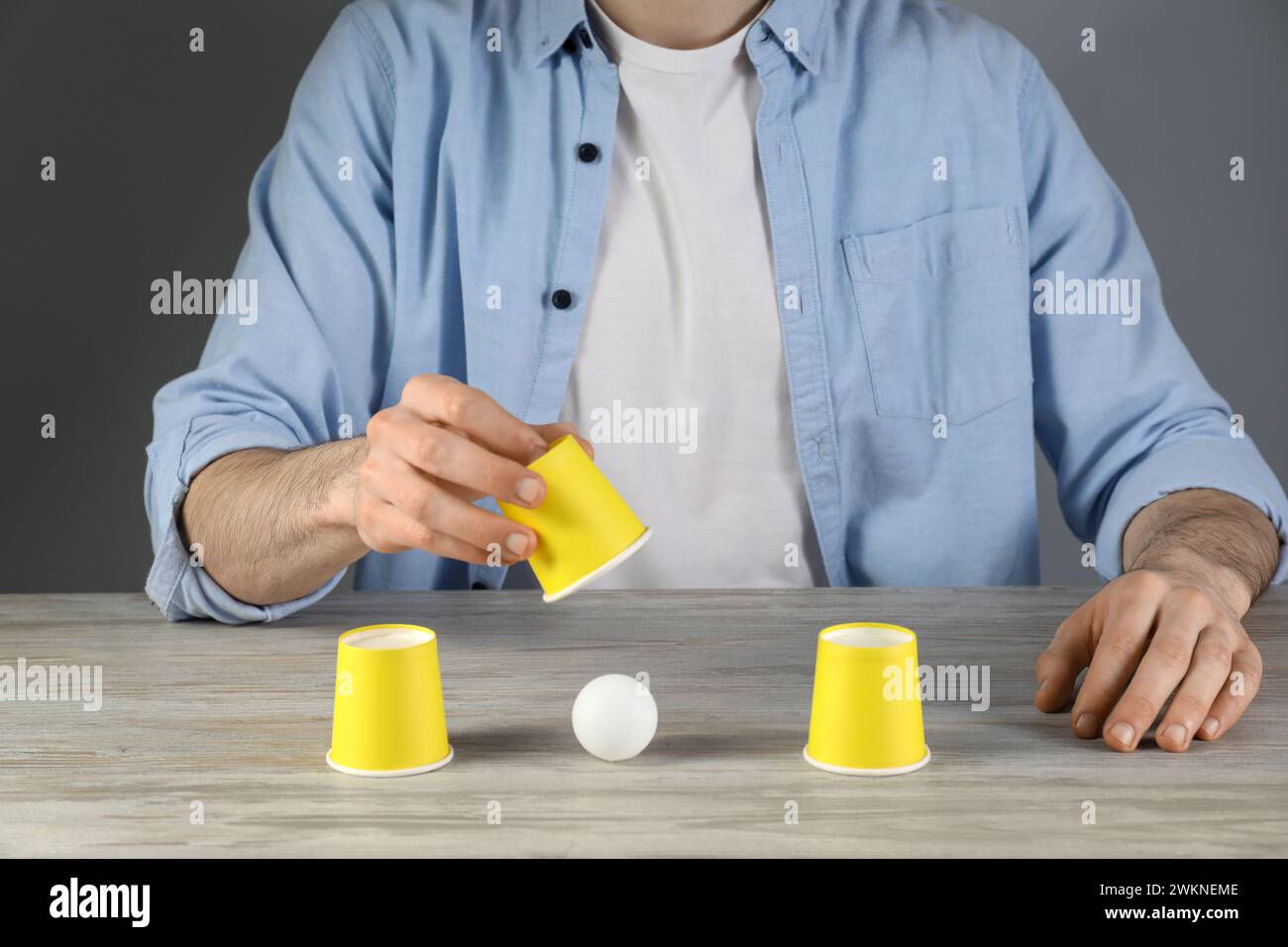 Shell game. Man showing ball under cup at wooden table, closeup Stock Photo