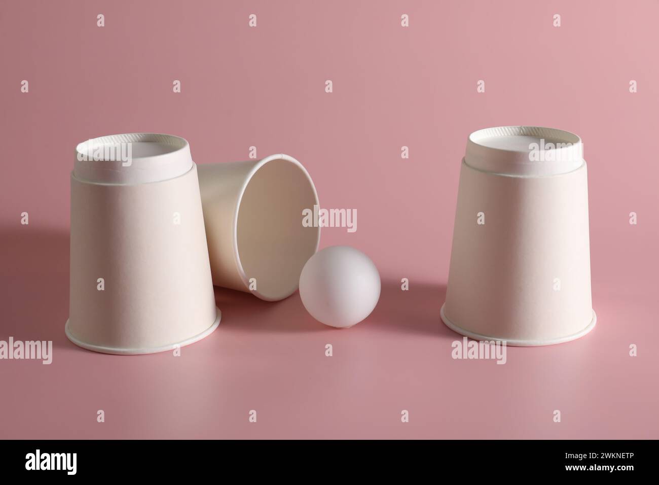 Shell game. Three paper cups and ball on pink background Stock Photo