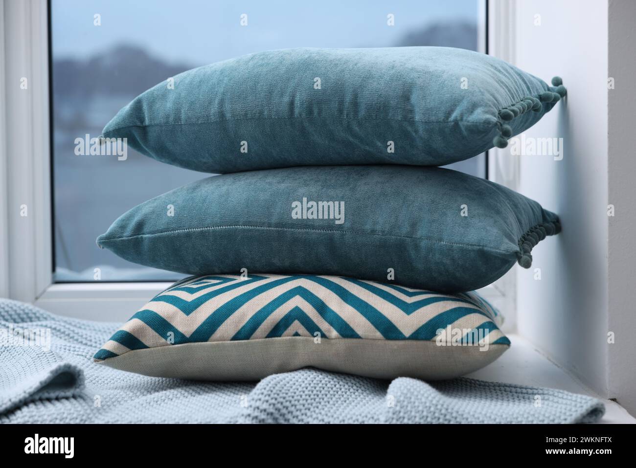 Stack of soft pillows and blanket on window sill indoors Stock Photo