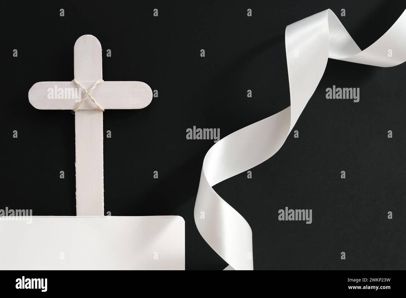 White wooden memorial cross with white ribbon in black background. Stock Photo