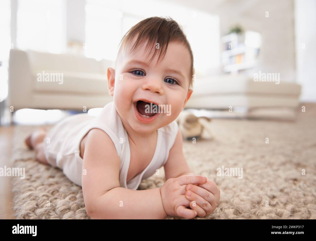 Happy, baby portrait and tummy time on floor, laugh and play in living room. Teething, child development and growth learning to crawl by laying on Stock Photo