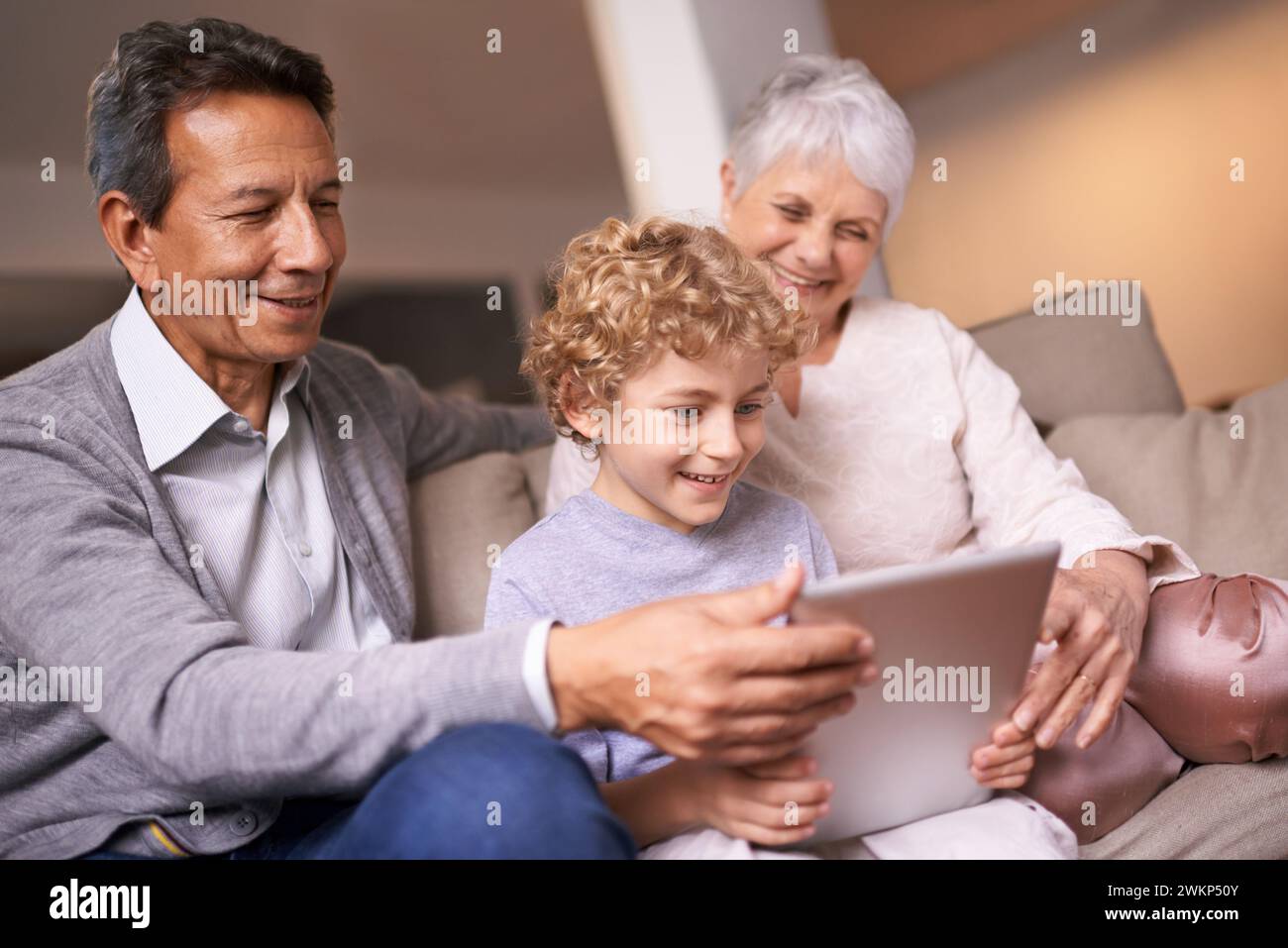 Happy family, grandparents and little boy with tablet for entertainment, social media or research on sofa at home. Grandma, grandpa and child smile on Stock Photo
